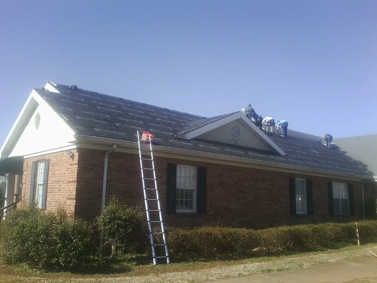 Crew tearing shingles off a brick ranch roof with a ladder set — Emergency Roof Repair work by our crew in New Market