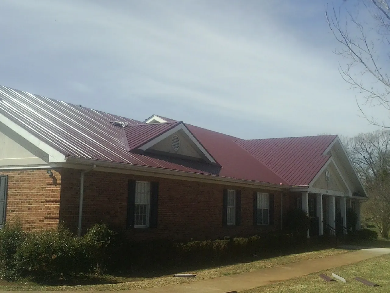 Red metal roof with gabled entries on a long brick building, from a Hail Damage Roof Repair job in New Market