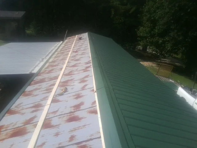 Old rusted panels beside newly installed green metal roofing — Wind Damage Roof Repair by Roofing Brothers in New Market