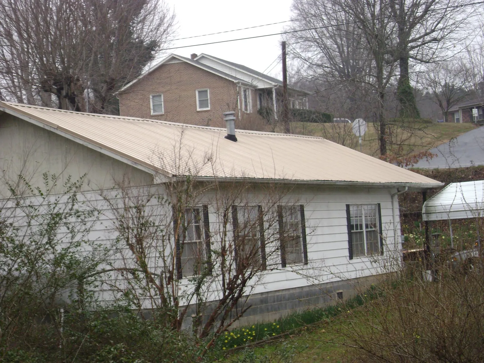Tan metal roof on a white sided house set into a hillside — Commercial Roofing by Roofing Brothers in New Market